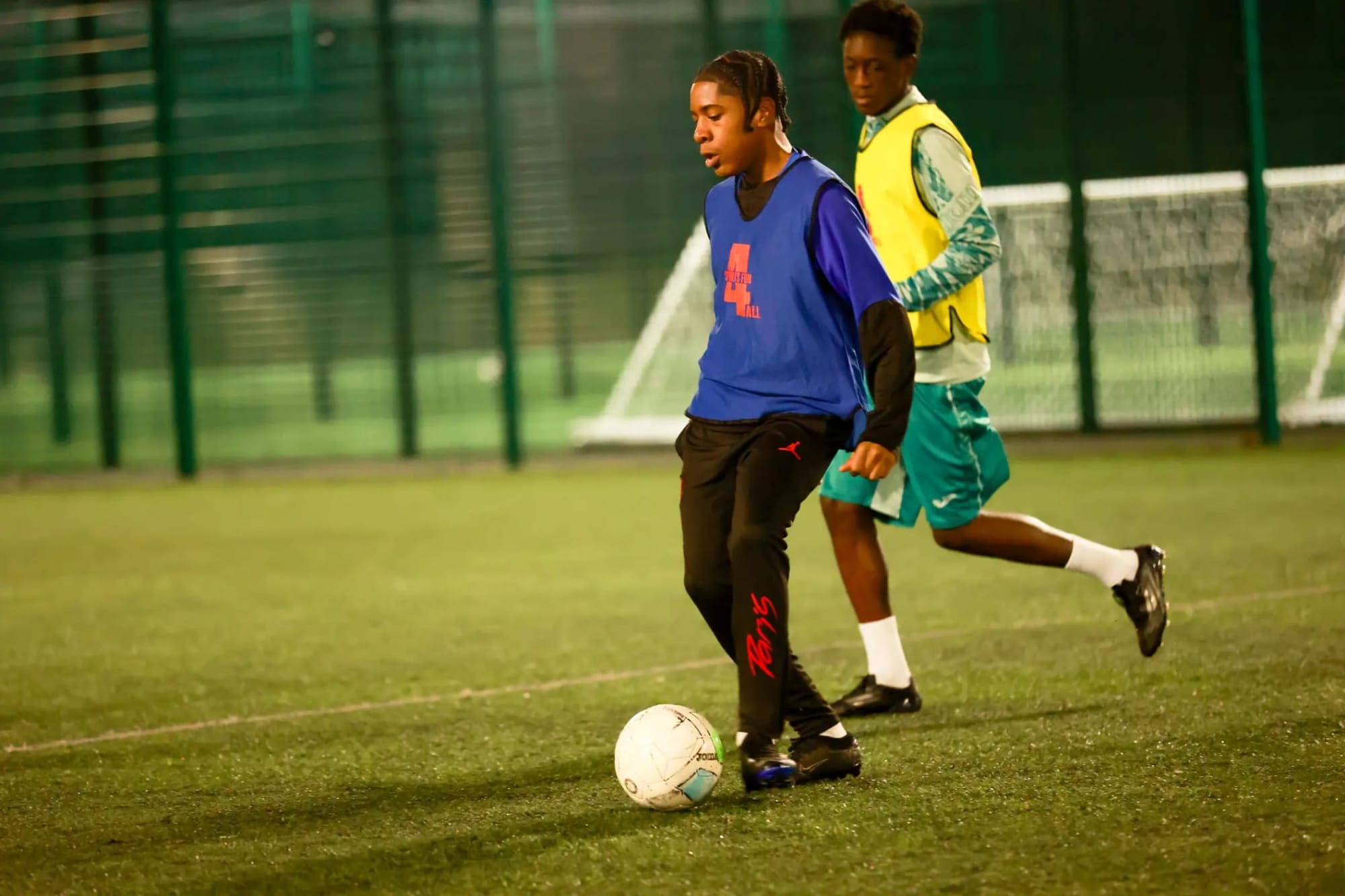 Two young footballers playing on floodlit pitch
