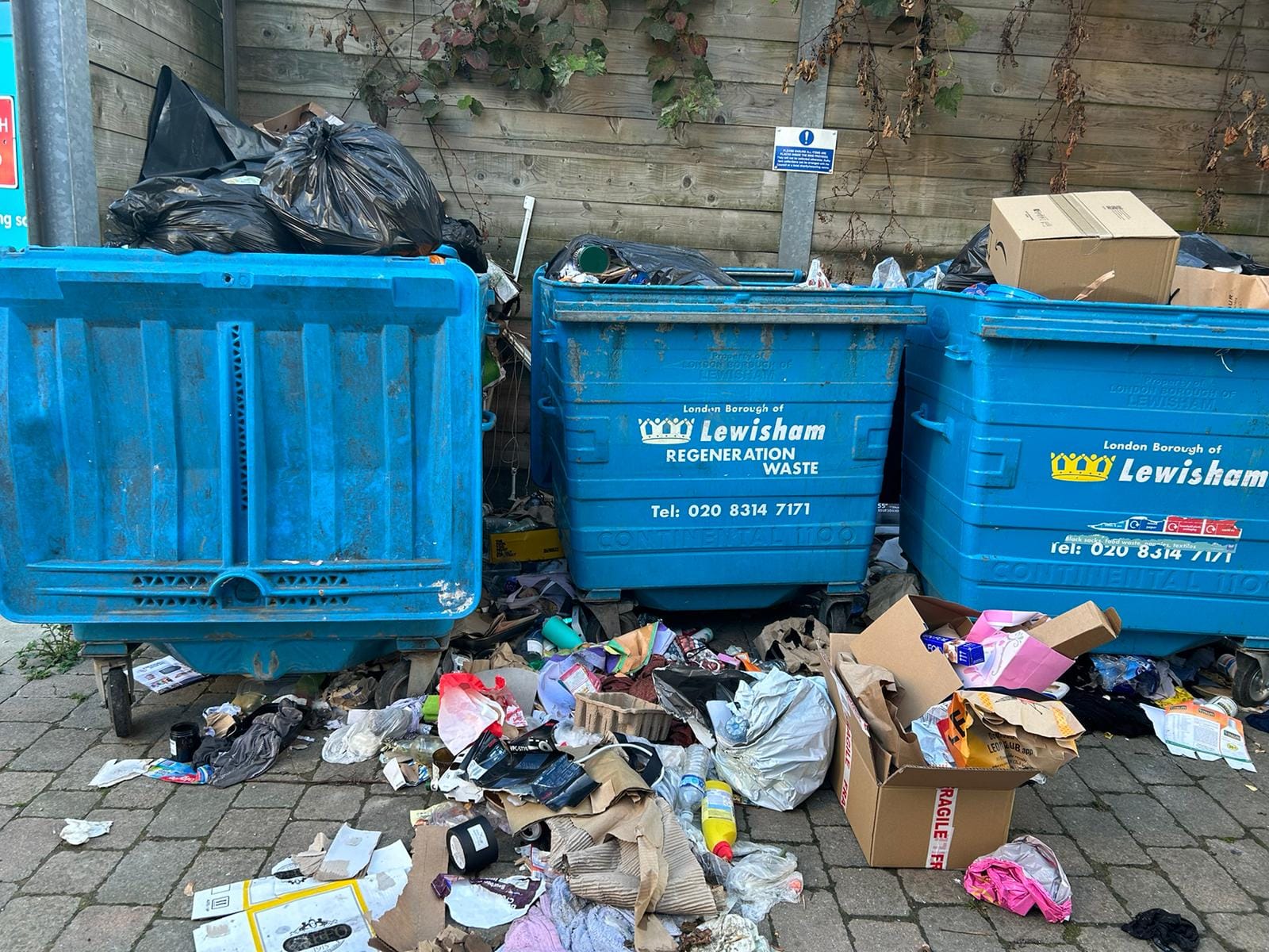 Three overflowing bins with rubbish strewn around them