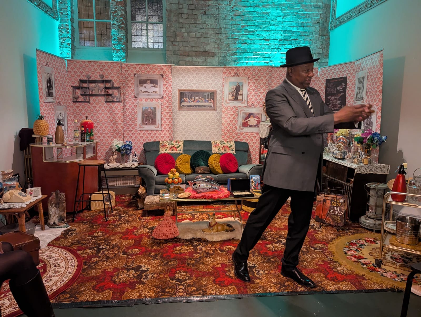Tony Fairweather in double-breasted jacket and trilby storytelling from the recreated living room.