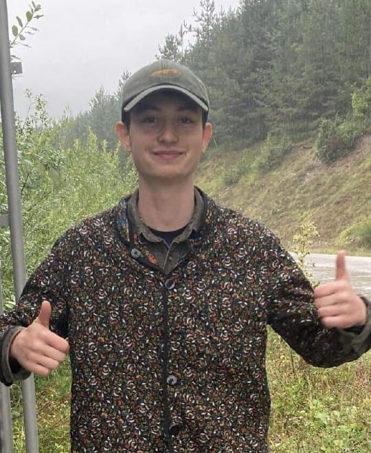 Jon Cink near a forest, smiling and doing thumbs up with both hands.