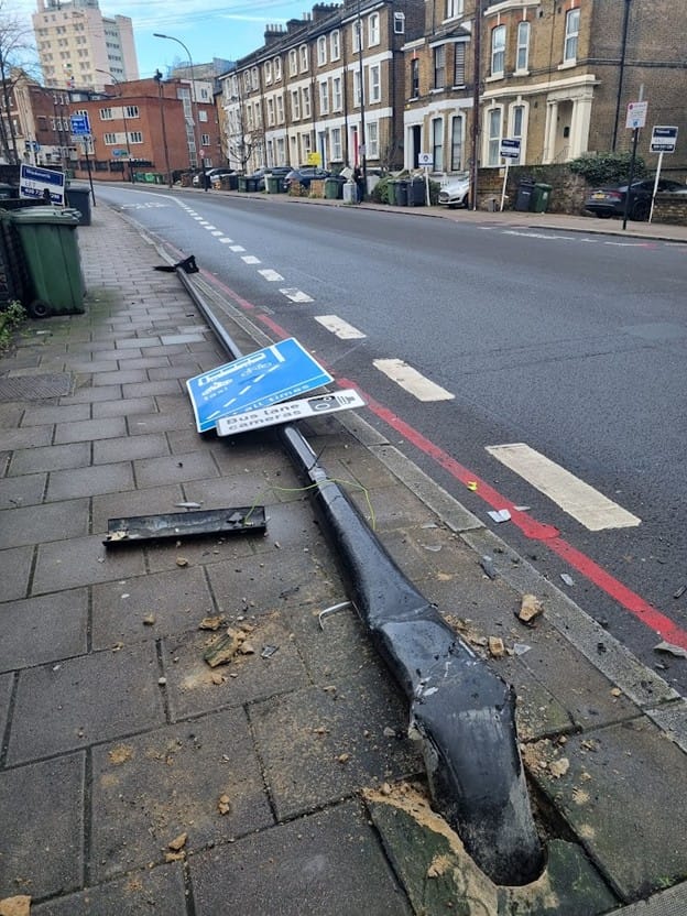 Road sign for bus lane which has been damaged in a collision, now lying on pavement.