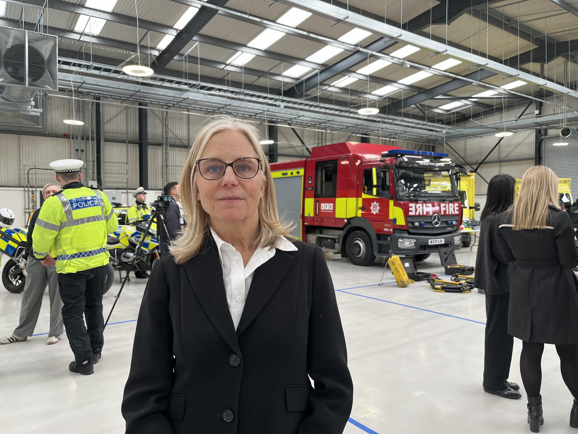 Photo in garage/hanger, Lily Matson in foreground, fire engine and police in background