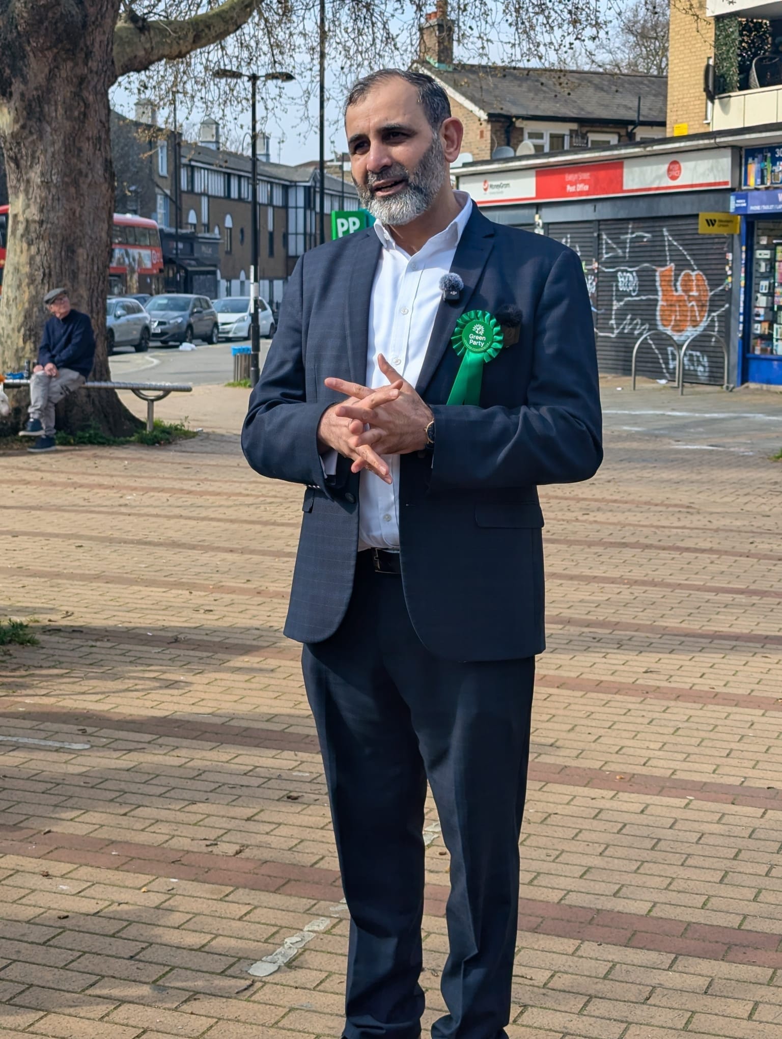 Tauseef Anwar addresses the crowd, Evelyn Triangle shops and traffic behind him.