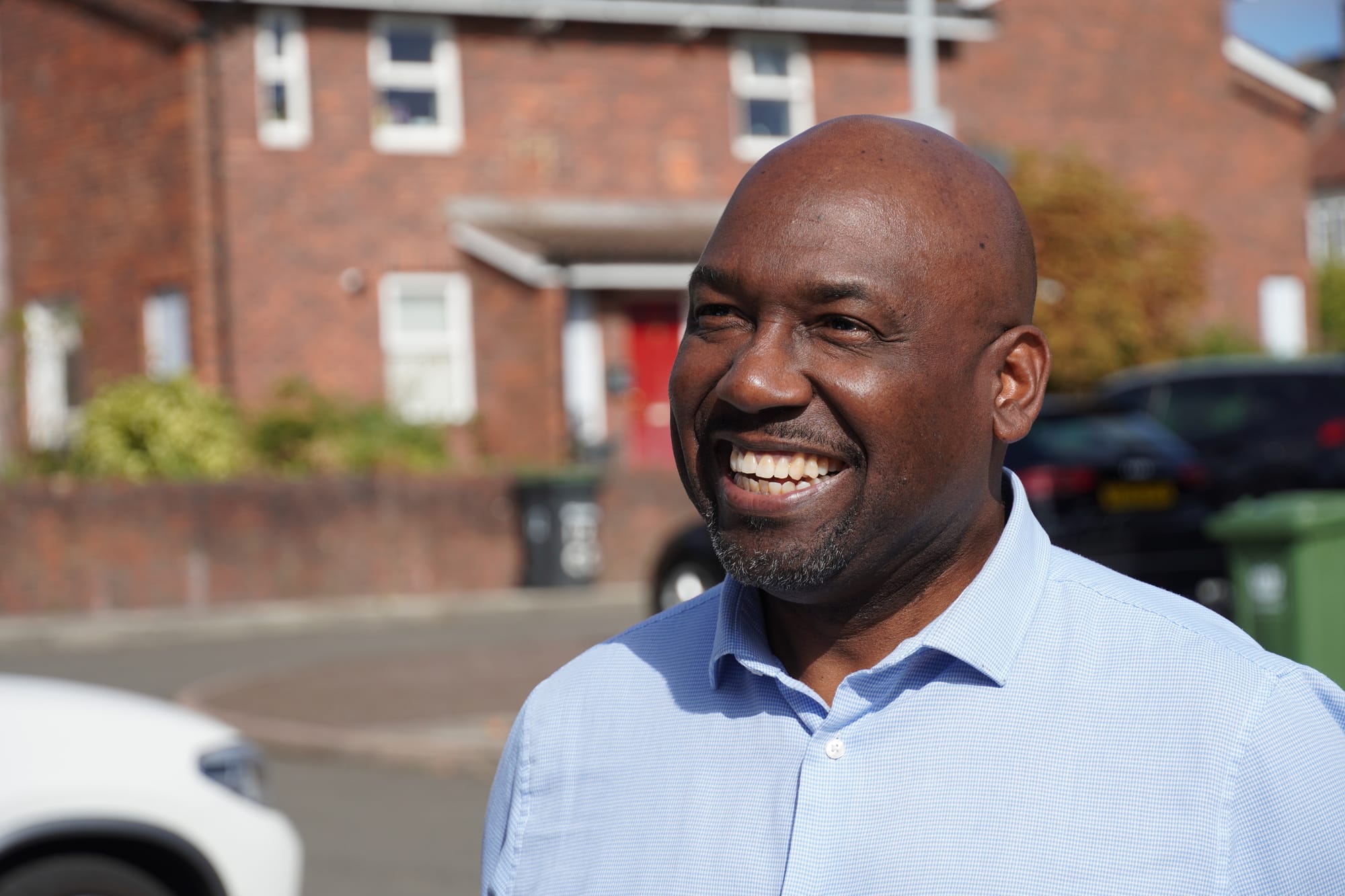 Man smiling, red brick houses behind him. 