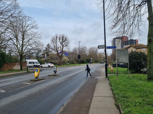 A small child crosses Sanford Street to reach Cold Blow Lane on their way to school. Wide road with no marked crossings. 