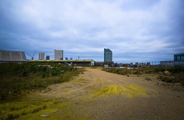 View of the empty site, with a wide gravel path through scrub, river visible. 