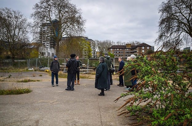 Residents and campaigners listening to developer representatives at site visit 27 March. Standing on broken concrete, budlea and weeds growing.