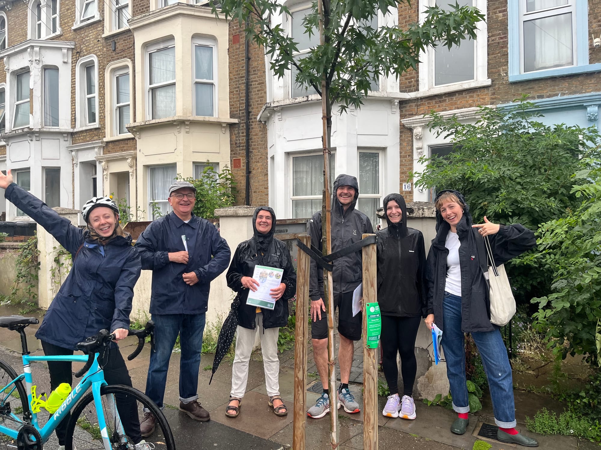 Volunteers in rain shower grinning and pointing at just planted tree.