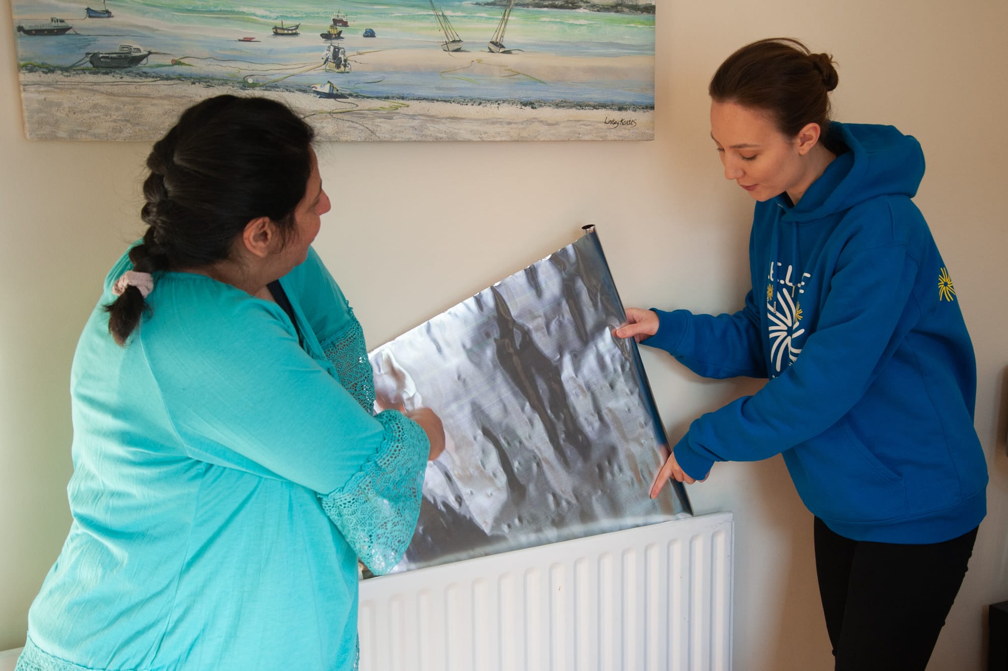 Two women Installing radiator reflector foil behind a radiator.