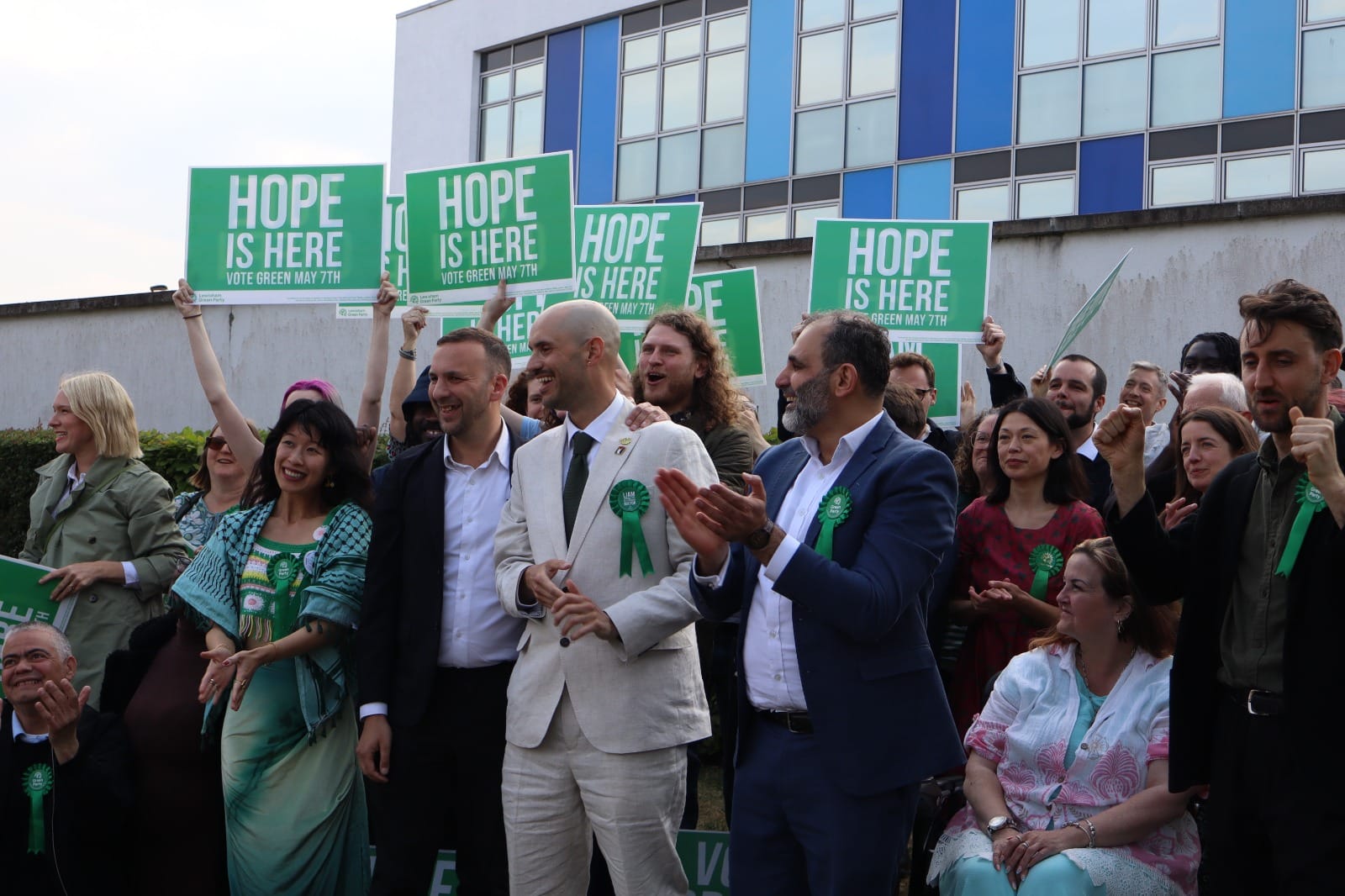 Zack Polanski, Liam Shrivastava and crowd of supporters holding signs "Hope is here".