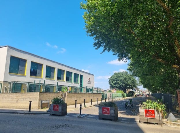 Image of Twin Oaks primary school street, blocked with planters. It is now closed to cars full time, and a new zebra crossing was installed opposite.