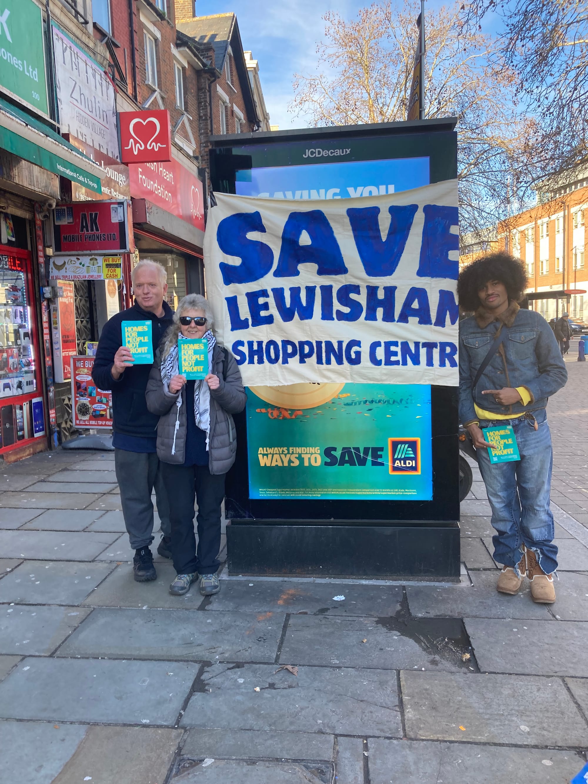 3 campaigners with flyers and large banner "Save Lewisham Shopping Centre".