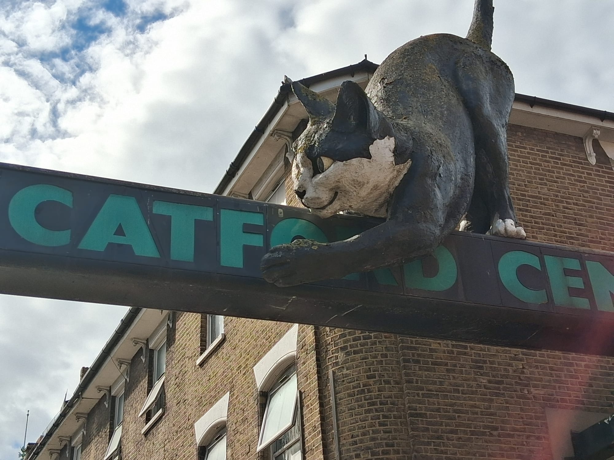 The Catford Cat - a large plaster and painted sculpture, paint peeling, perched on an aging sign for Catford Centre.