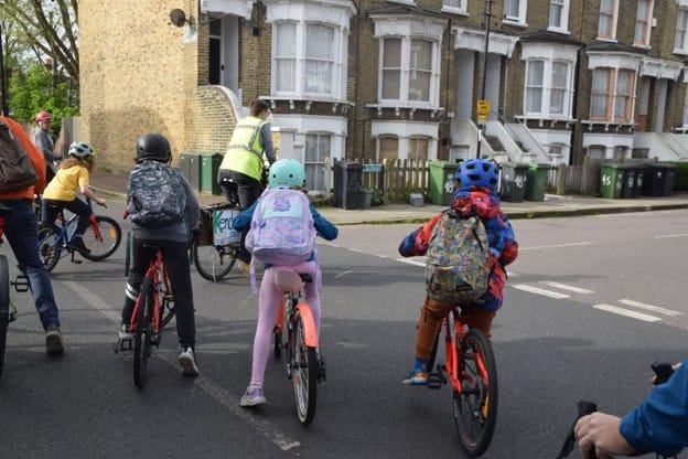 Children on bikes wearing backpacks, with an adult leader in hi vis - the New Cross bike bus which utilised pedestrianised Cold Blow Lane
