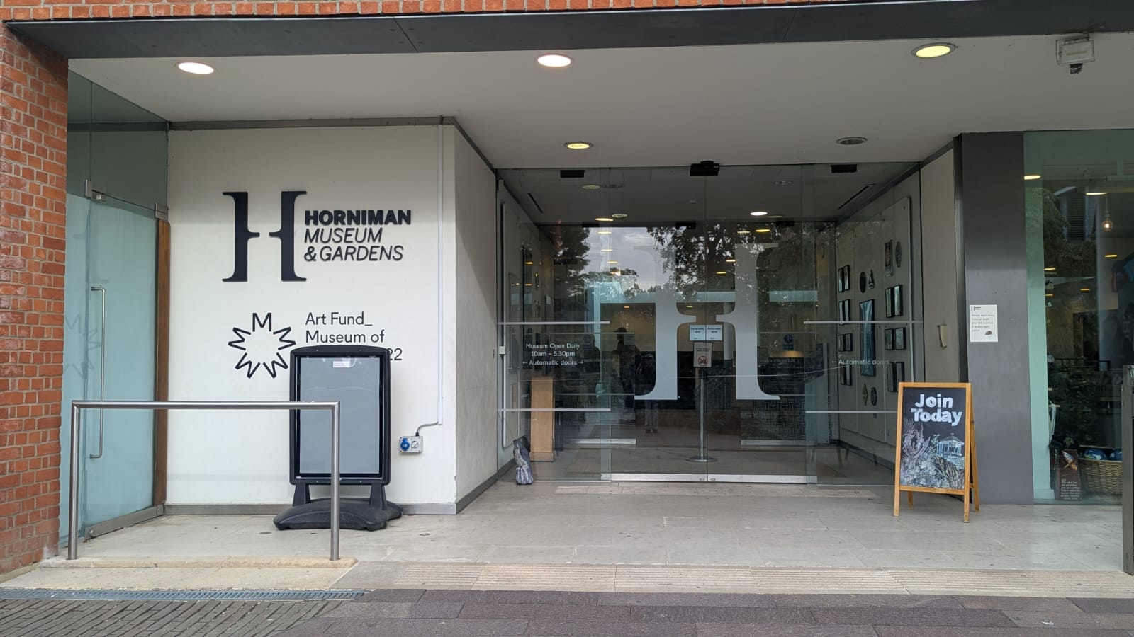 Museum entrance, glass doors of foyer with logo, blackboard stand on pavement with words "join today".
