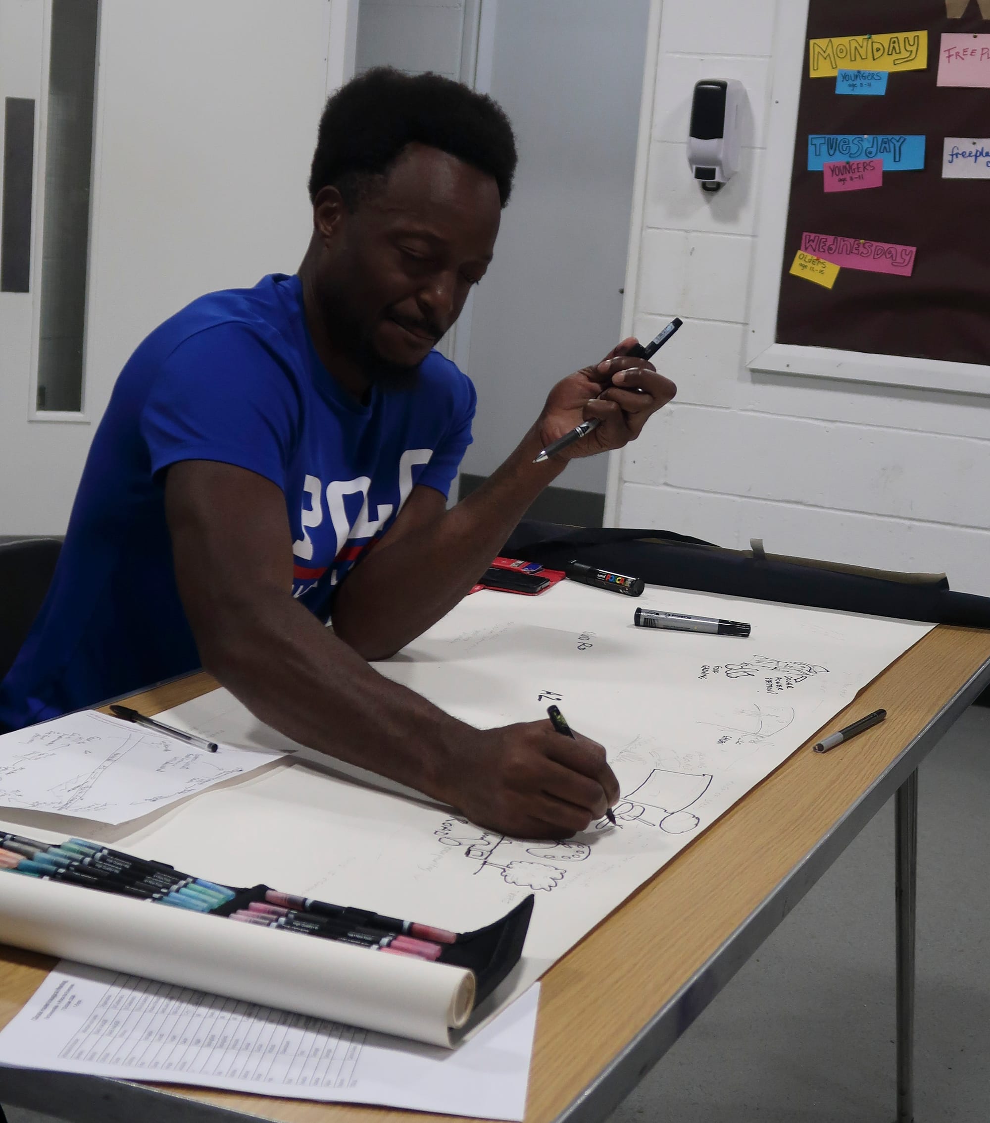 Artist beginning to sketch out the map, roll of paper on tresell table. 