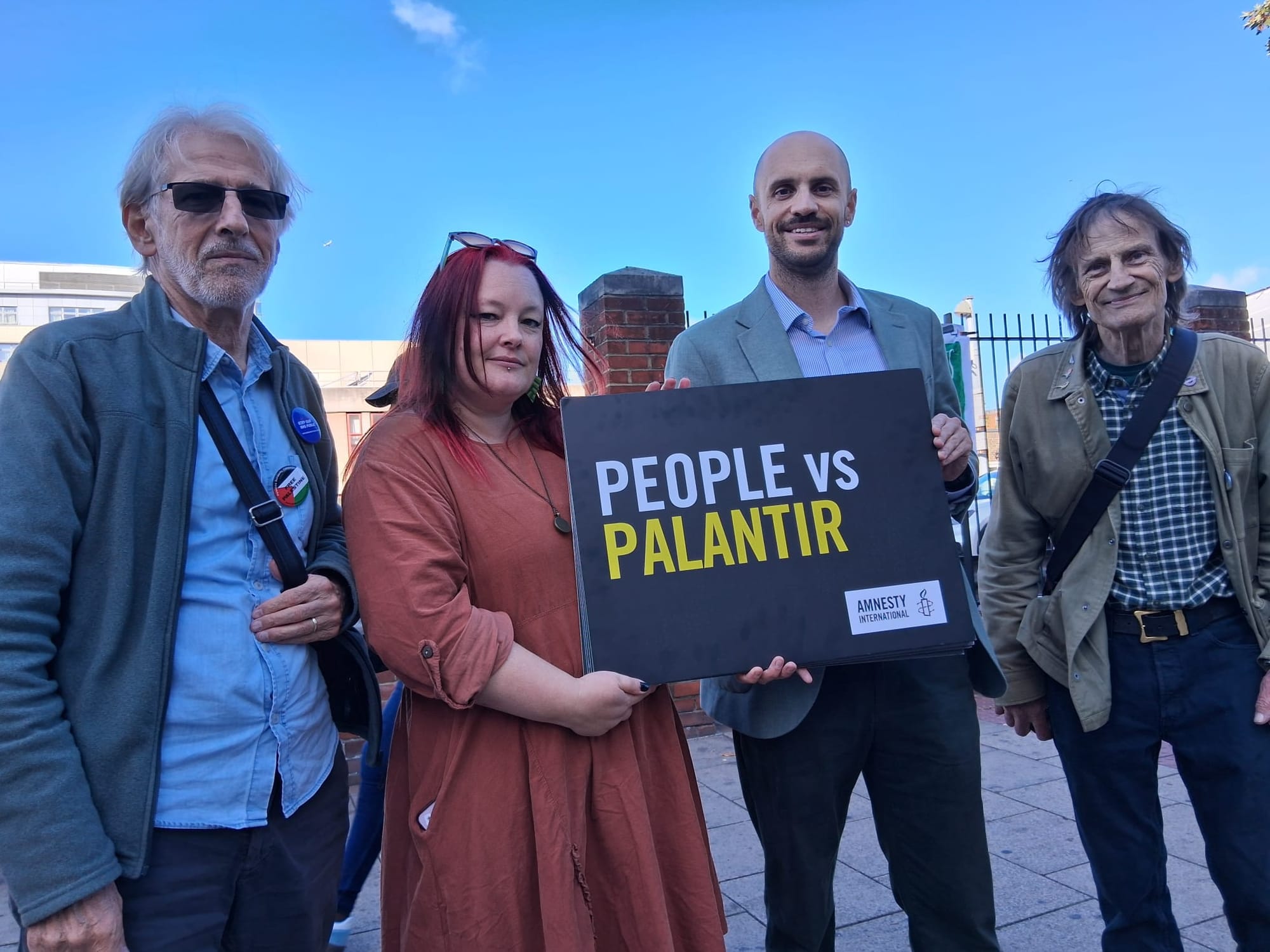 Gardiner and the mayor Shrivastava holding sign "People vs Palantir" campaigners at each side.