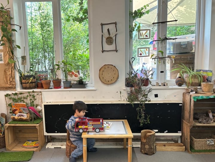 Parents describe the nursery as "warm, welcoming and inclusive" - child playing at low table, plants strewn inside and in ga