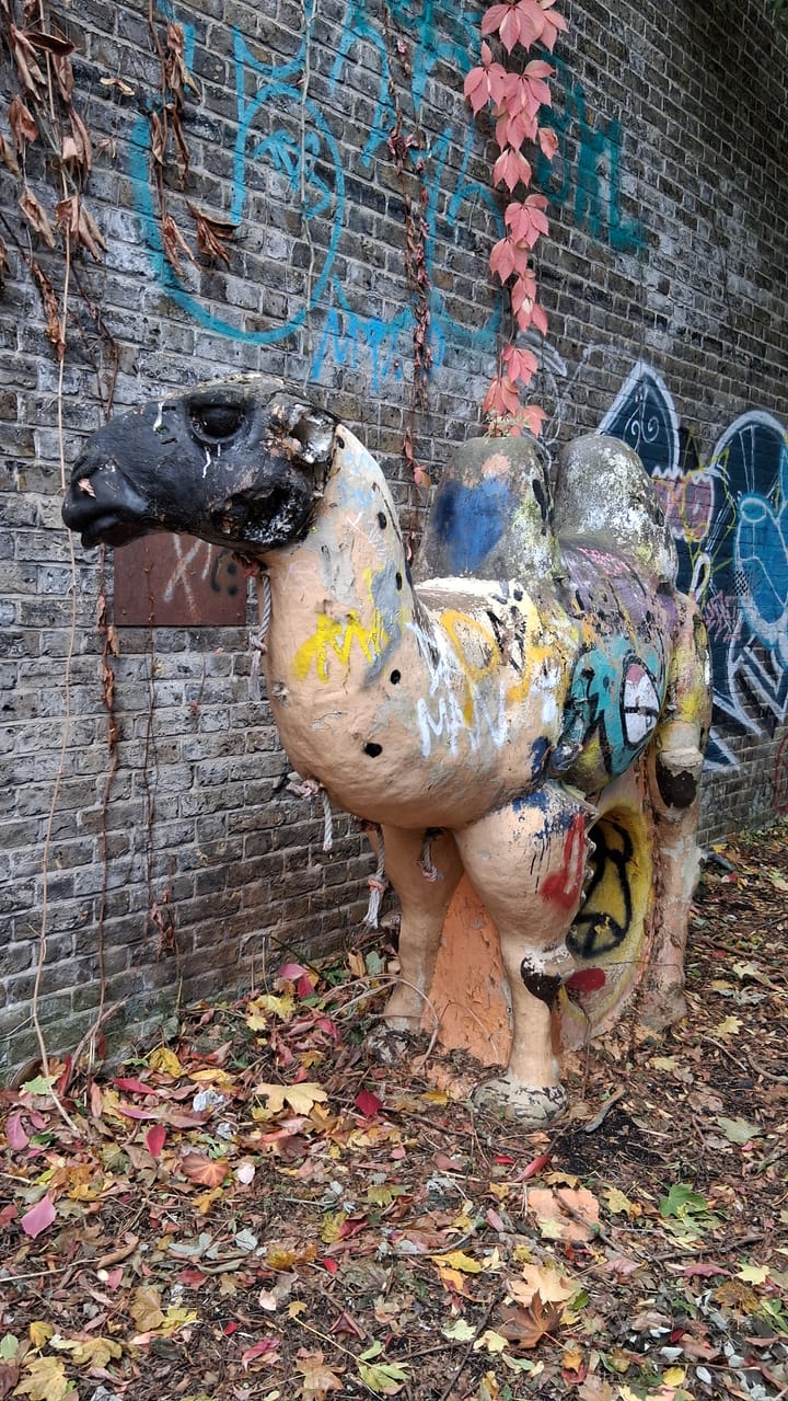            A statue of a camel, with peeling paint and covered in graffiti, left in an abandoned playground on the site.