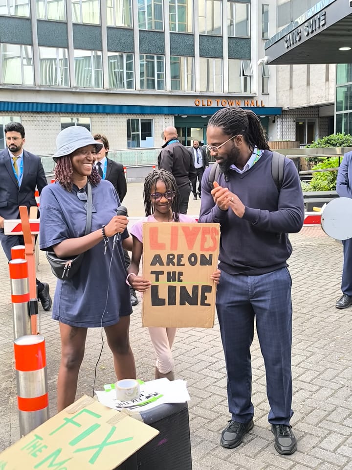 Mica holding microphone, her child with placard "Lives are on the Line" and her husband, all smiling, at protest