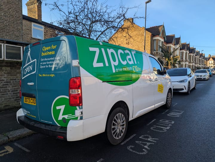 Zipcar van parked in car club bay with words "Open for Business" on the back.