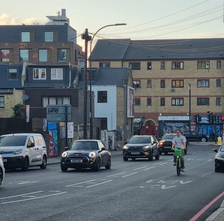Cyclist navigating Amersham gyratory in early evening with stream of cars in next lane,