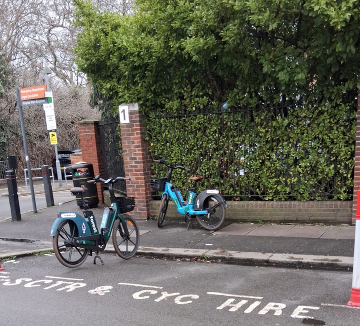 Two Forest bikes at Albacore Crescent outside Lewisham Hospital, one parked in the marked bay, one on the pavement. 