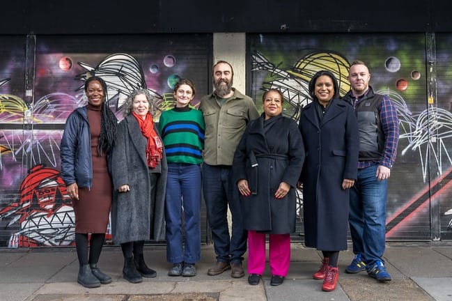 Holly and Asher from The Castle Cinema with Janet Dabey MP, Mayor Brenda Dacres and councillors standing outside grafitti covered shutters. 