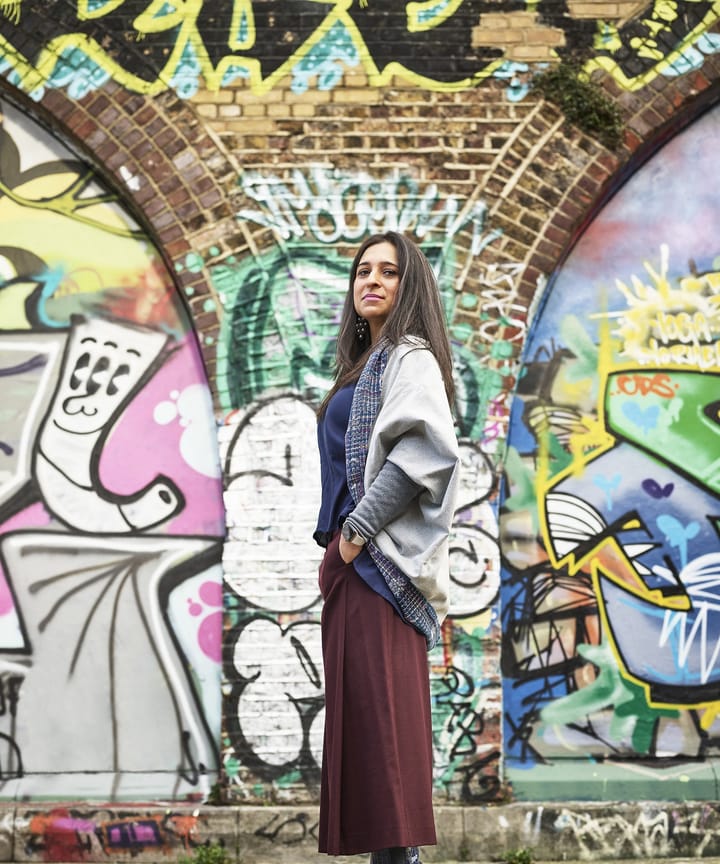 Rupa Ganguli smiling and standing in front of graffiti covered arches in Deptford.
