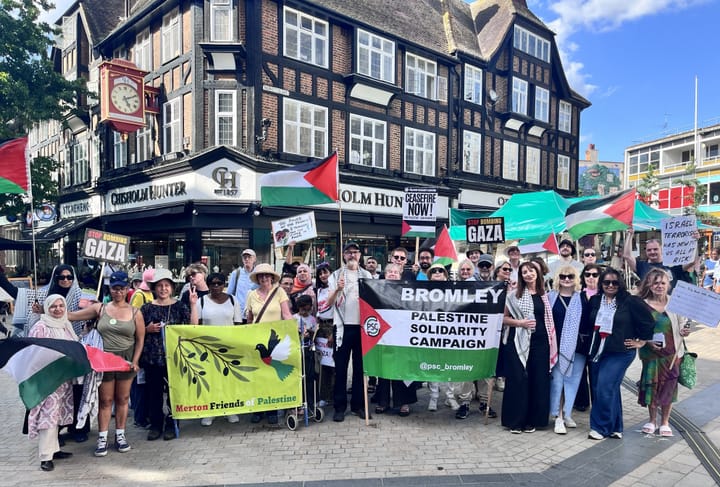 Large group standing on pavement in Bromley with keffiyas, Palestinian flags and banner "PSC Bromley". 