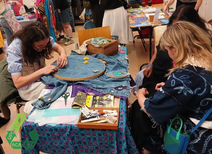 People sewing at a table, part of the free clothes mending session with Make Mee studios.