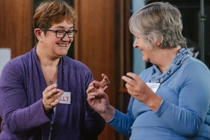 Instructor and participant both smiling with raised hands doing finger exercises