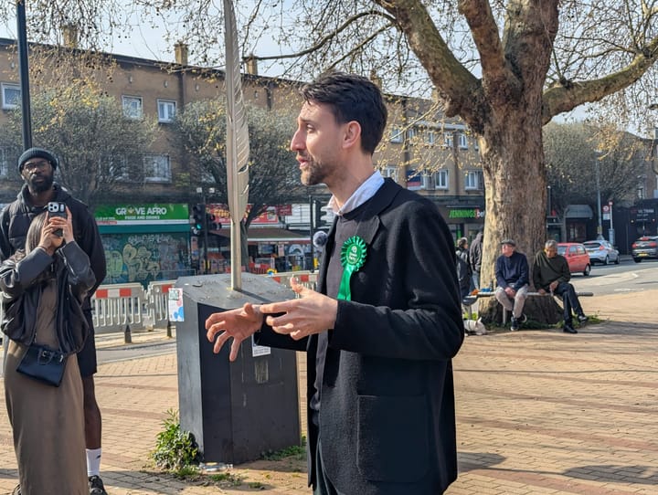 Rudi Schmidt speaking to crowd at Evelyn Triangle, with John Evelyn memorial feather statue behind him.