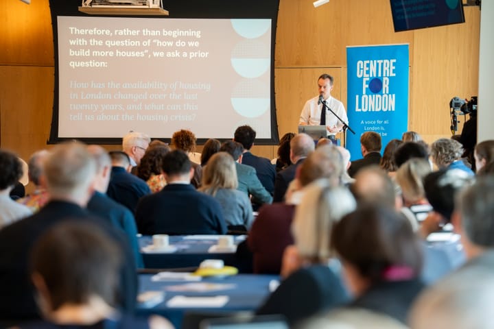 Man in shirt and tie showing slides on screen to audience in front of banner "Centre for London". 
