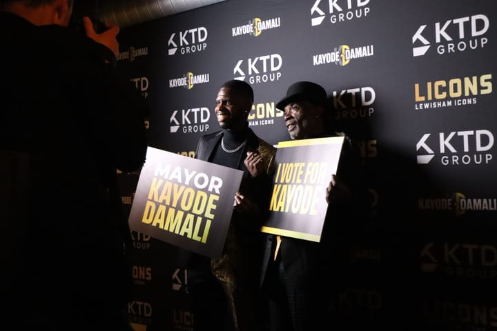 Kayode and a supporter holding signs: Mayor Kayode Damali and I vote for Kayode.