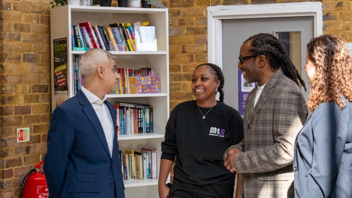 Sadiq Khan meets youth worker and Wayne James - all beaming - at Marcus Lipton centre, brick walls and book shelf behind them.