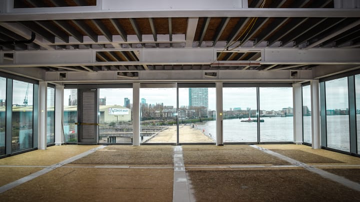View of site through windows of glass building - the only building that has been built. Convoys Wharf sign visible through window