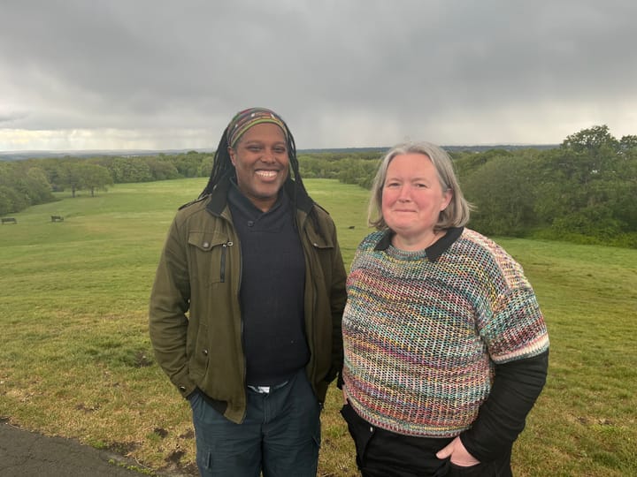 Man and woman smiling, green parkland behind them. 