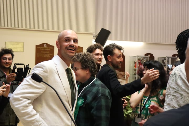 Liam Shrivastava grinning and surrounded by scrum of supporters. 