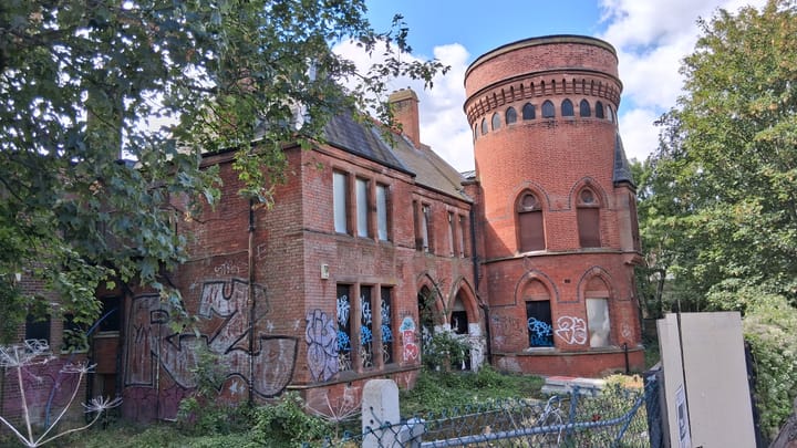 Victorian brick building covered in grafitti with overgrown trees around.
