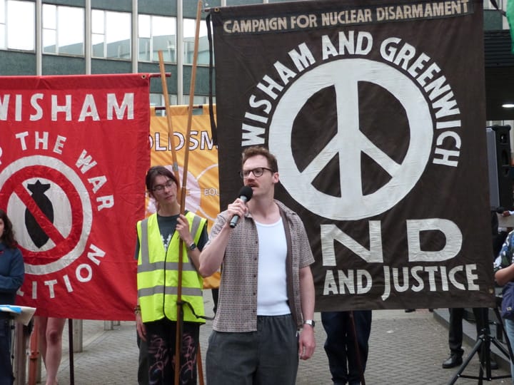 Ed Sutton with microphone speaking at a rally at Lewisham Town Hall, July 2025. CND and Stop the War banners behind him.