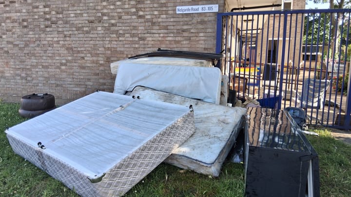 5 mattresses, camp bed and fridge freezer left dumped on grass outside gates of housing development. 