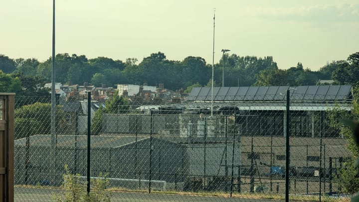 Large air pollution monitor with cylinders and mast visible between buildings at Kings College sports field, with the pavilion behind. 