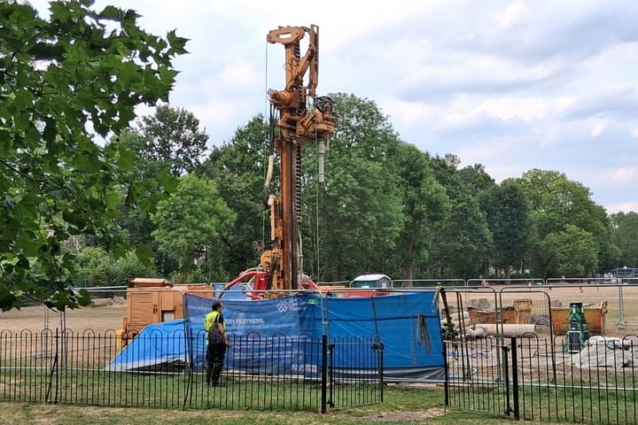 Drilling rig near play park, skips visible behind. 
