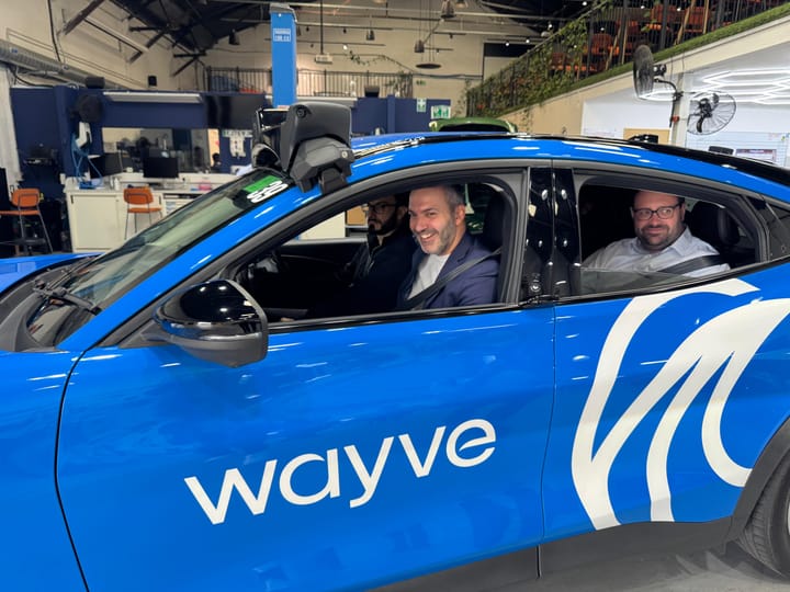Bassam Mahfouz AM and Thomas Turrell AM sitting in stationary Wayve vehicle and smiling, at depot. 