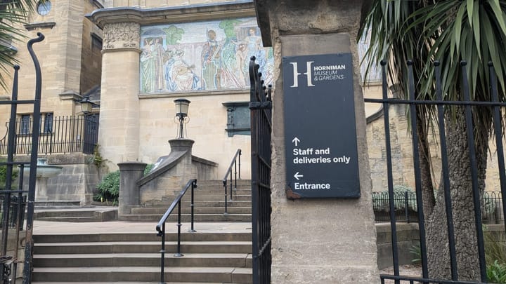 Staff entrance to Horniman Museum with sign.  Mosaic on wall of Victorian building and iron gate.