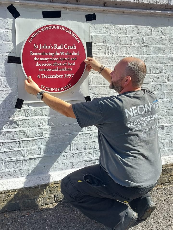 round plaque being fitted with words: St John's rail crash. Remembering the 90 who died, the many more inured and the rescue efforts of local services and residents. 4 December 1957