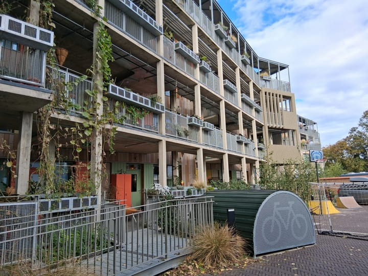 4 story wooden-framed building with balconies, walkways and hanging vines, wooden shutters on doors and cycle hanger at the front. 